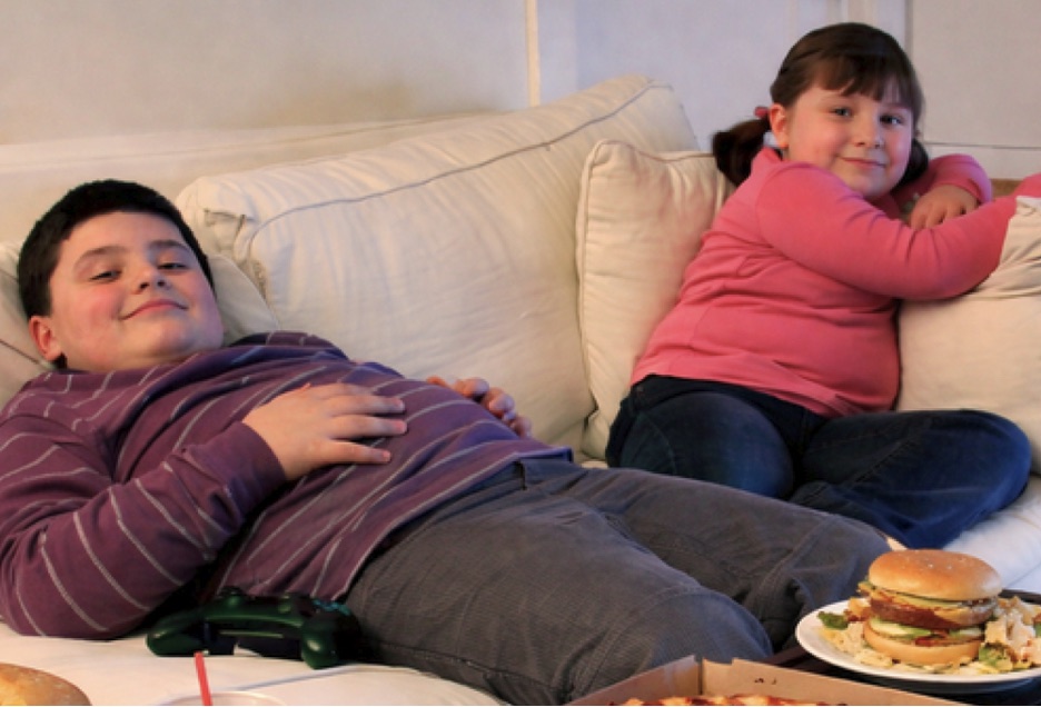 Overweight children sitting on couch with unhealthy snacks
